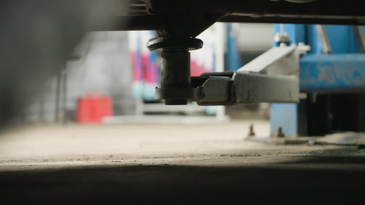 Close-up de elevador automotivo eletrônico elevando um veículo em uma oficina mecânica, com equipamento mecânico azul visível ao fundo, destacando a precisão e estabilidade do mecanismo de elevação.