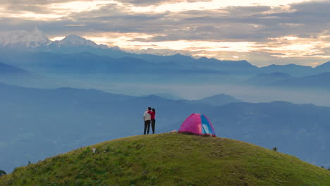 drone shot of a couple hugging each other while viewing nature's serenity early morning rise mountains horizons and landscape camping above hills of shailung dolakha nepal beauty