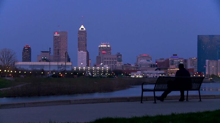 A man sits on a park bench overlooking the city of Indianapolis at dusk