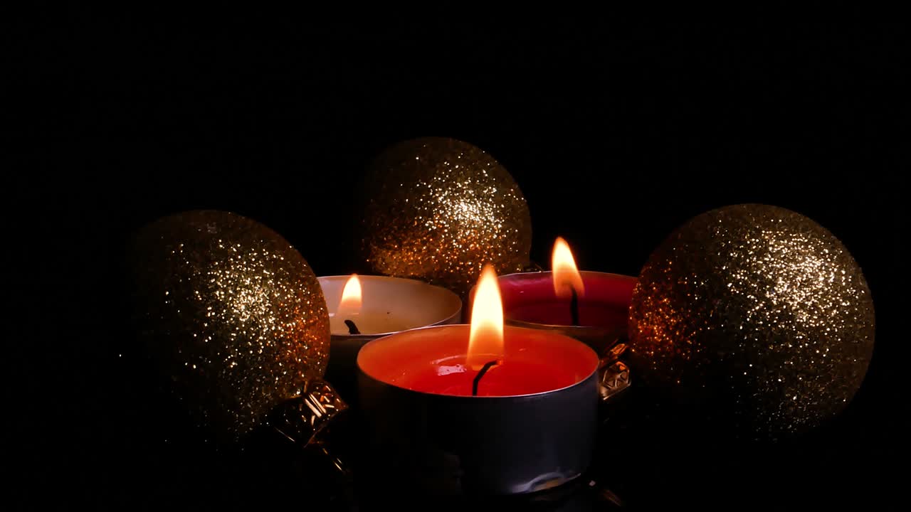 Fiamma di candela natalizia e palline decorative al buio. Buon Natale. Festività di Capodanno. Vacanze invernali. Fiamma di candela di cera. Oscurità notturna. Giocattoli dorati. Video