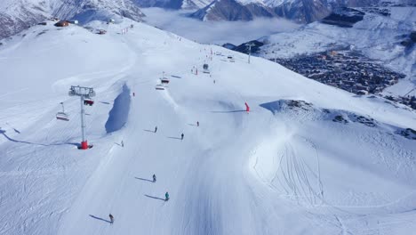 aerial gimbal down revealing several skiers skiing down a snowy mountain slope in the alps