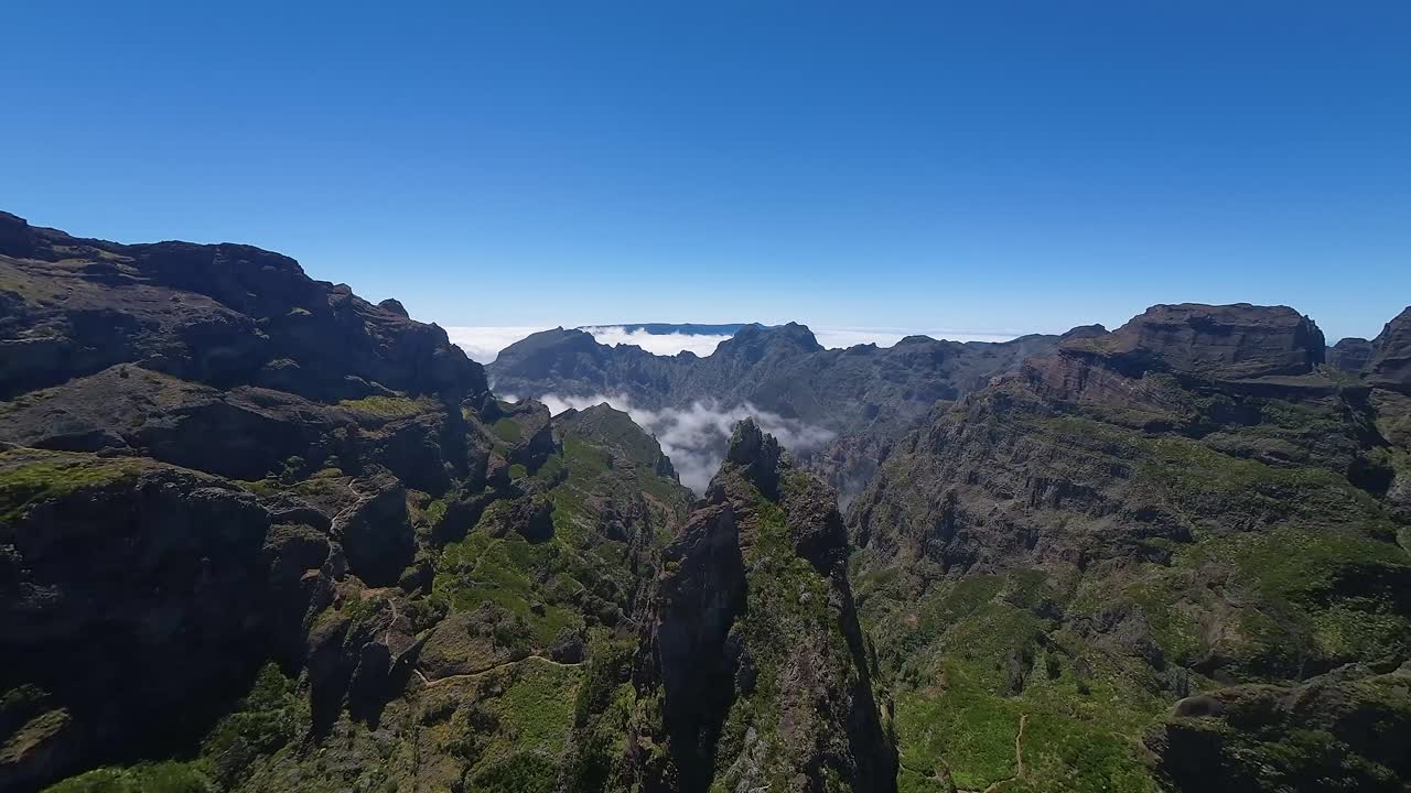 Deep green valleys with low clouds and rugged terrain of Madeira. Aerial view of Pico do Pico hiking trail and park.