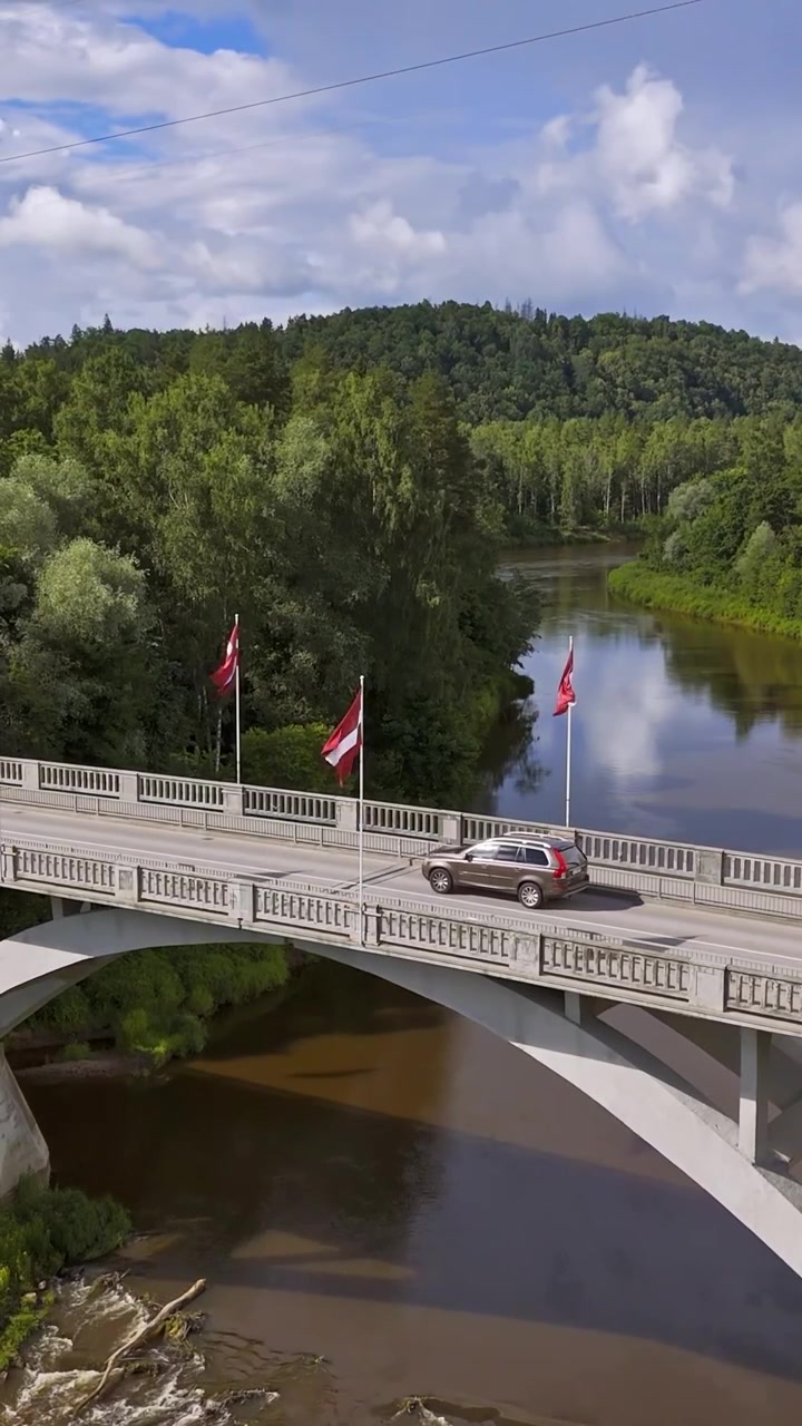 Ponte ad arco mentre le auto attraversano il fiume Gauja vicino a Sigulda, tra colline boscose, ripresa aerea statica angolata