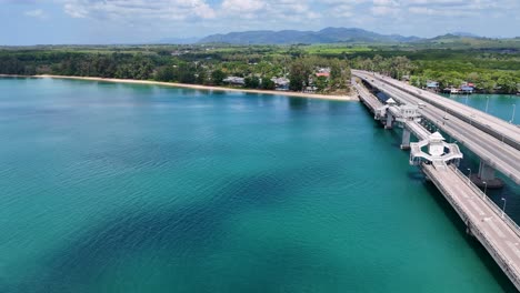 Drone footage captures Sarasin Bridge in Phuket, Thailand, spanning turquoise waters under clear skies, highlighting the scenic coastal landscape