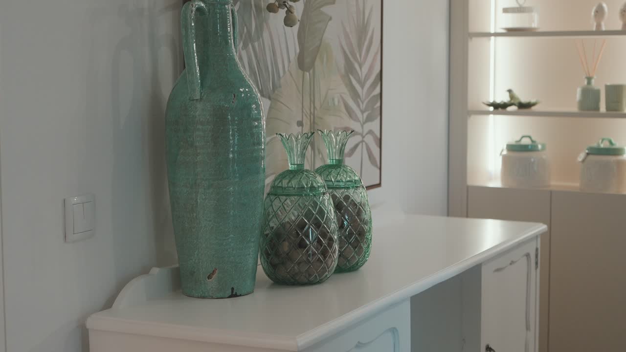decorative turquoise ceramic vase and pineapple shaped glass jars on a white sideboard