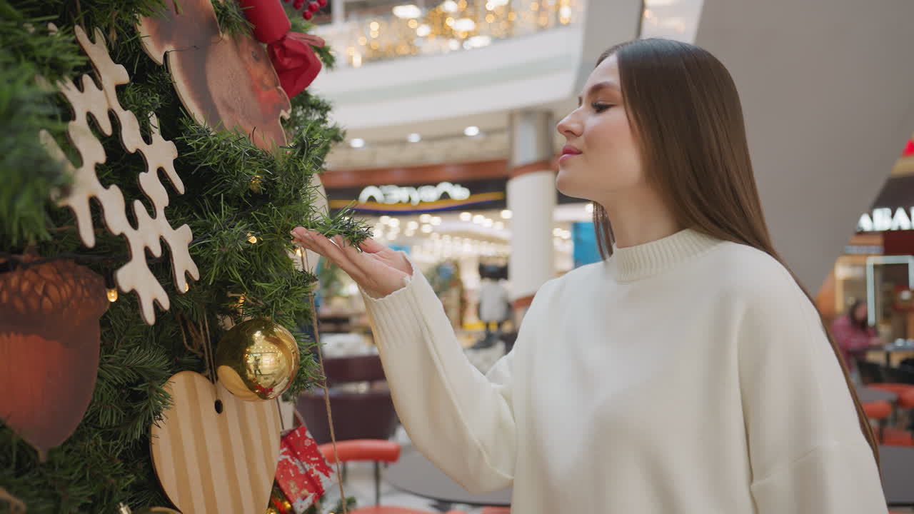 Side view of lady smelling decorative plant in shopping mall, with decorative lights in background, other people are visible in background