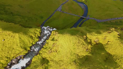 Scenic-aerial-view-of-a-huge-green-mossy-waterfall,-touristic-landmark-in-Iceland