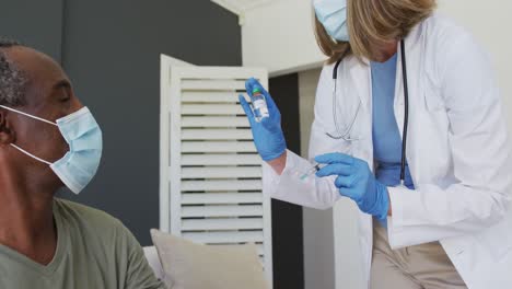 médica caucasiana sênior usando máscara preparando vacina para homem afro-americano