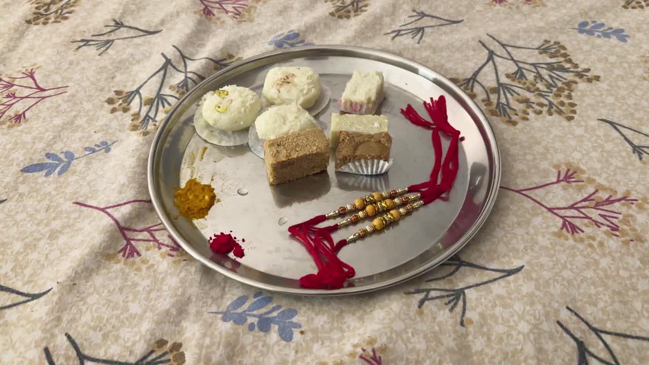 A thaali, arranged with various items for the Rakhi festival, The plate features an assortment of sweets and rakhi bracelets with red threads and gold beads, accompanied by turmeric and kumkum powder