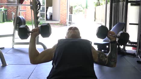 muscly man in home gym exercising incline chest press dumbbell