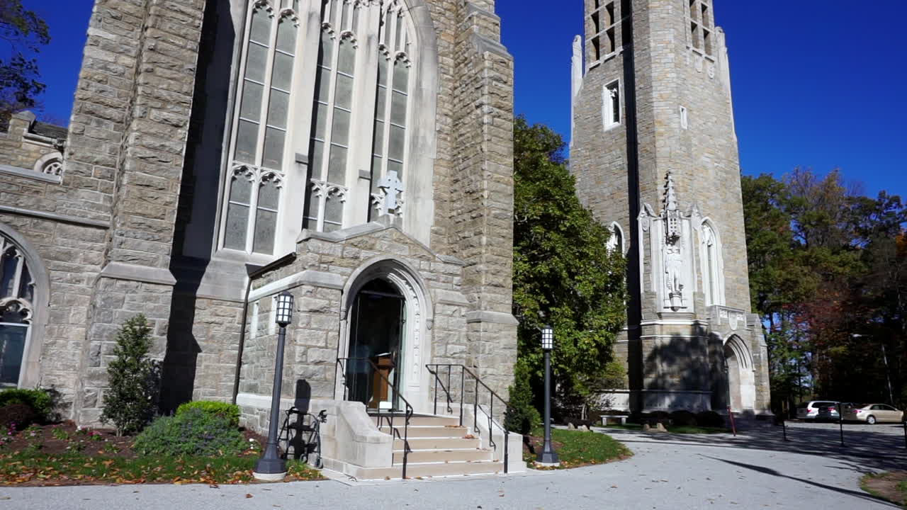 Gothic style bell tower and church facade with stained glass window.  Camera tilts down to entrance.