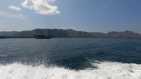 pov mirando a través de las aguas con olas creadas por lanchas rápidas que pasan junto a veleros cerca de la isla de komodo