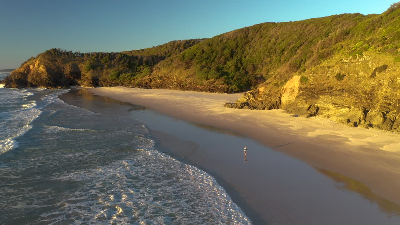 hombre caminando por la playa de arena en la cabeza rota cerca de byron bay