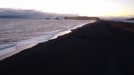 a tranquil black sand beach at reynisfjara, iceland, stretches into the distance, reflecting the soft hues of a sunset or sunrise over the calm north atlantic waters