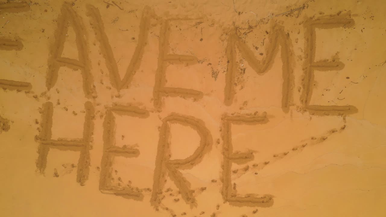 Aerial view of a desert beach with waves braking with a funny inscription in the sand saying Leave me Here. Rising Drone Shot