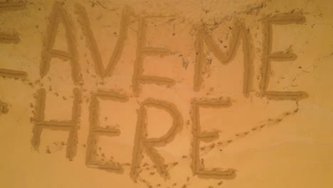 aerial view of a desert beach with waves braking with a funny inscription in the sand saying leave me here. rising drone shot
