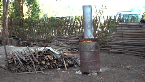 wood piles and active burn barrel with fire during daytime on farm in chiang mai thailand