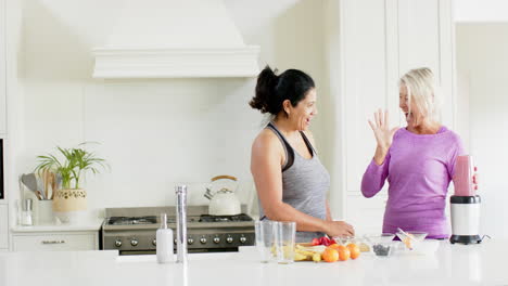 Dos-Mujeres-Mayores-Felices-Y-Diversas-Preparando-Cócteles-Y-Chocando-Los-Cinco-En-La-Cocina,-Cámara-Lenta