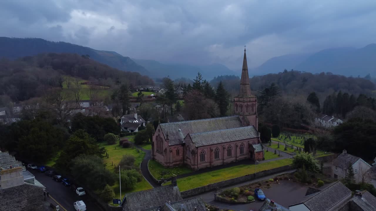 video aéreo de un dron 4k de una iglesia en un día nublado y sombrío con montañas en el fondo - keswick, distrito de los lagos