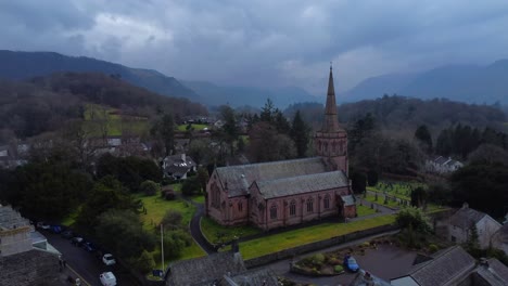Aerial 4K drone video of a church on a cloudy, gloomy day with mountains in the background - Keswick, Lake District