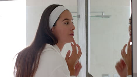 applying skincare, woman with headband looking in mirror in home spa setting