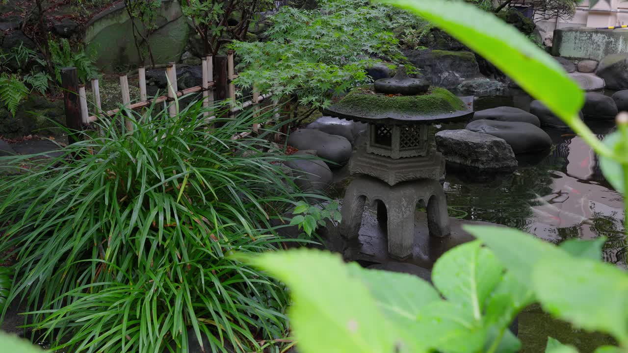 A tranquil scene of a traditional Japanese garden with a mossy stone lantern surrounded by lush green foliage and large rocks