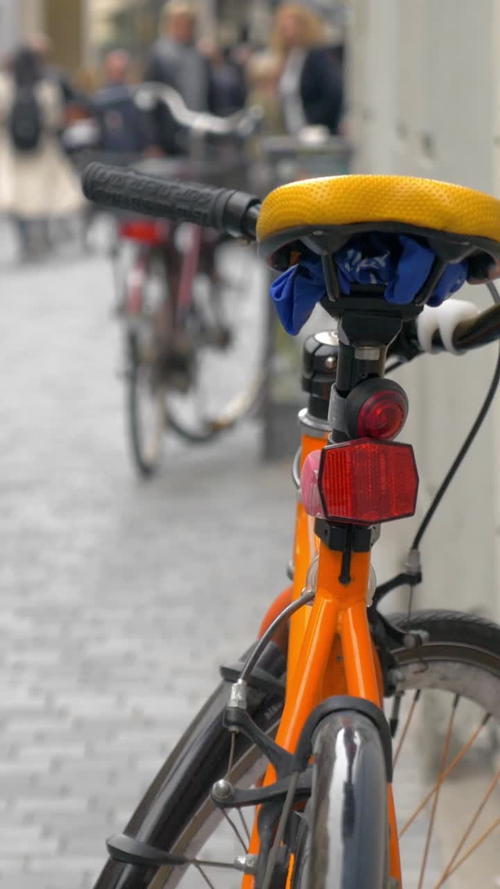 Bicicleta laranja com pessoas desfocadas caminhando em rua urbana.