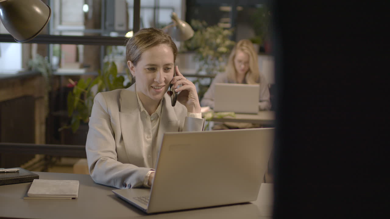 Businesswoman Talking On Mobile Phone And Working On Laptop Computer In The Office