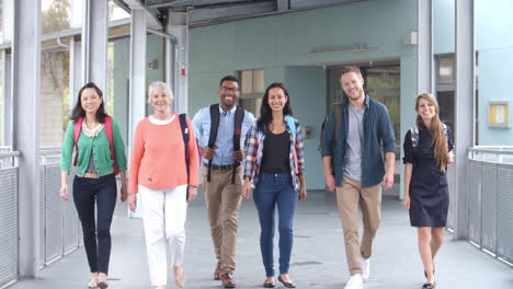 un grupo de maestros sonrientes caminan por un pasillo hacia la cámara