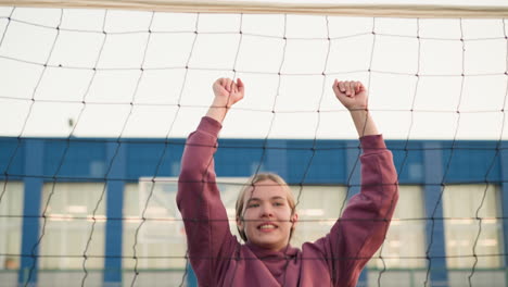 volleyball player jumps up and slams ball with powerful pose showing victory, focus on athlete's determination, background features volleyball net and buildings