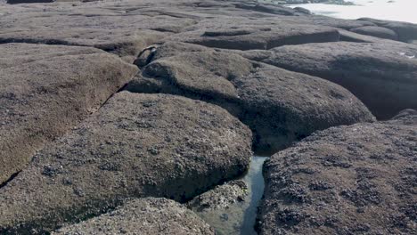 Flying-backwards-over-a-rocky-beach,-revealing-Fort-de-la-Crèche