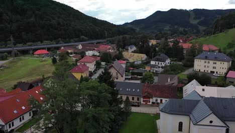 a drone lifts off from a small slovak village beneath dark blue skies, gradually tilting the camera downward for a sweeping aerial view