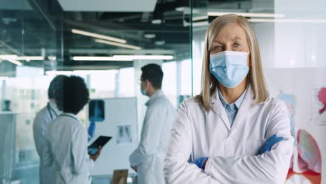 caucasian senior female doctor in medical mask looking at camera in hospital office