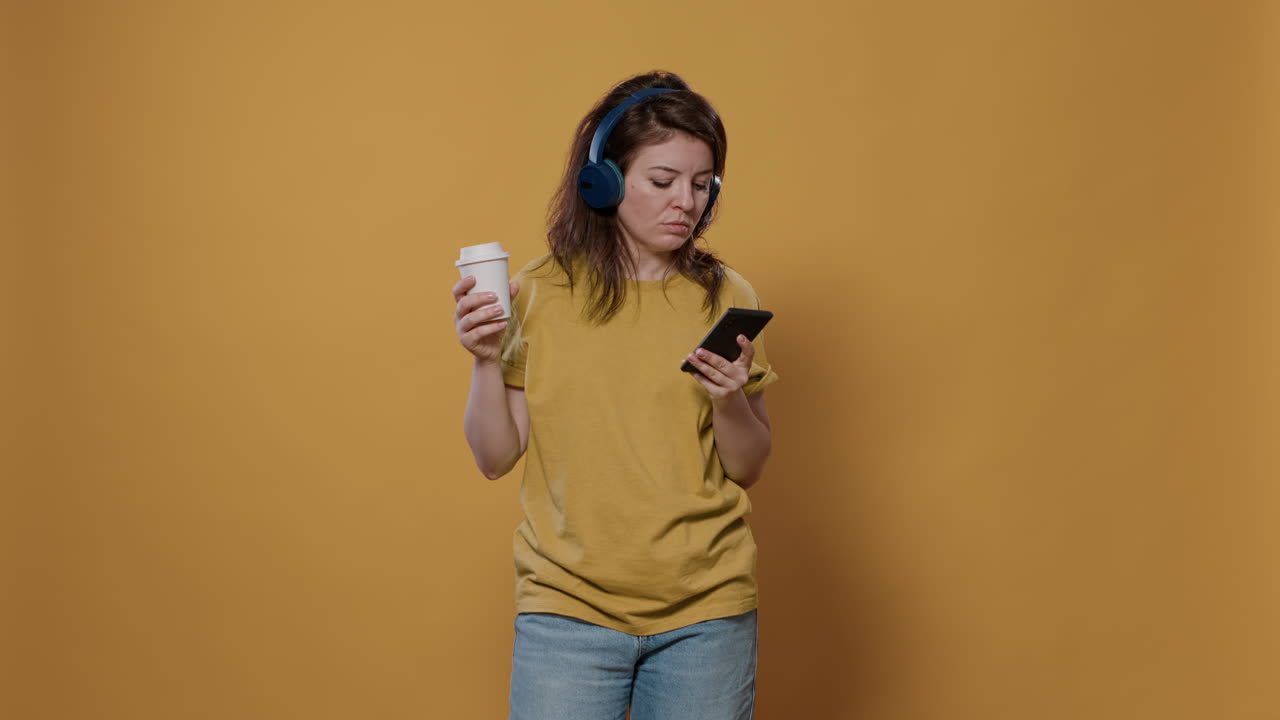 Woman listening to music with headphones and using a smartphone while holding a coffee cup
