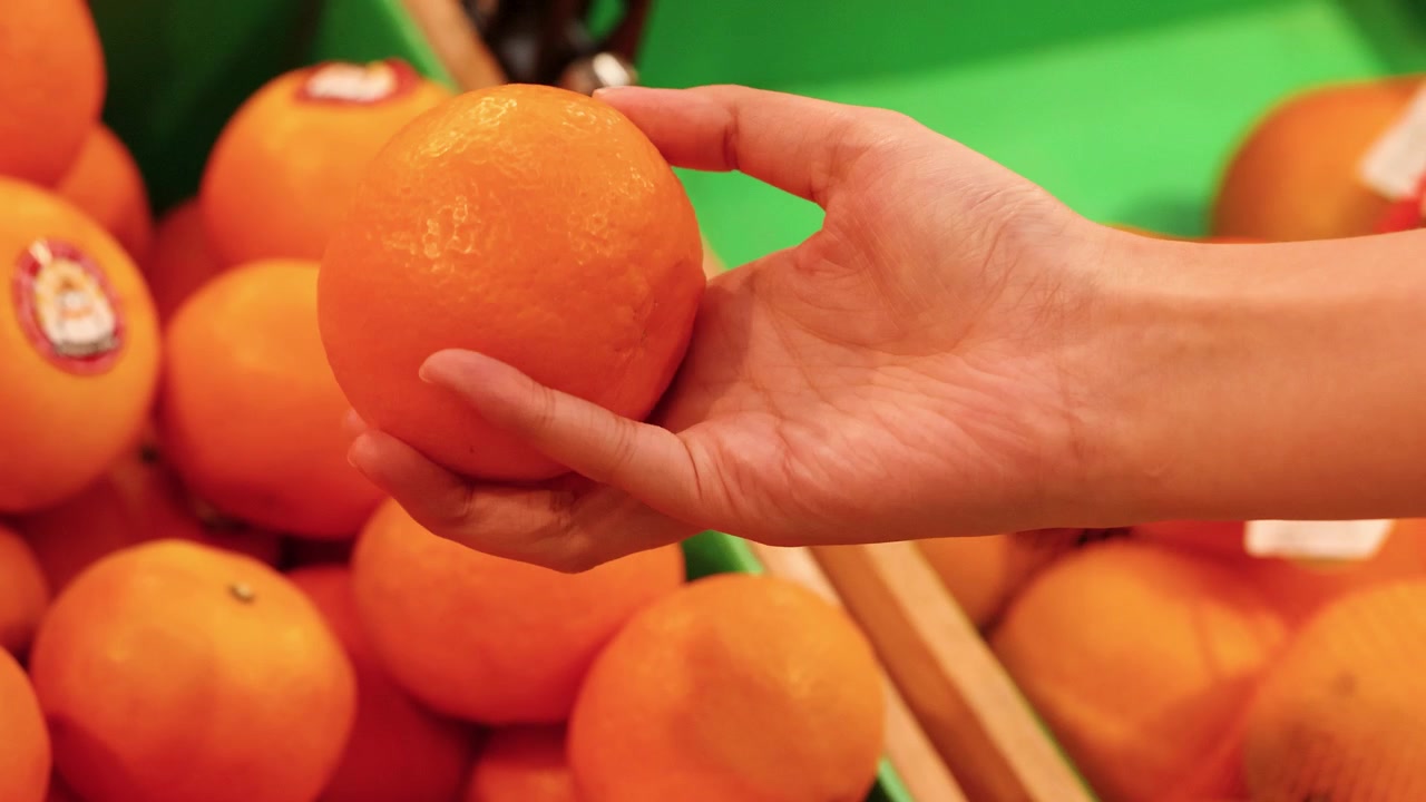 Close-up tangan memilih buah jeruk segar dari pajangan supermarket di Bangkok