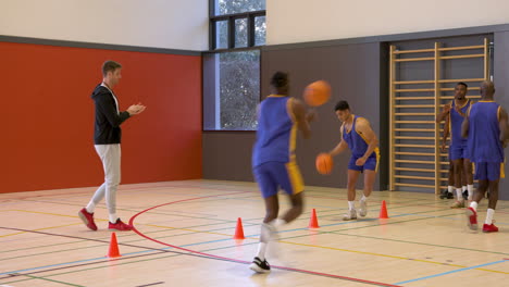 basketball players practicing dribbling skills in gym with coach encouraging