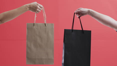 Video-of-hands-of-caucasian-women-holding-shopping-bags-with-copy-space-on-red-background