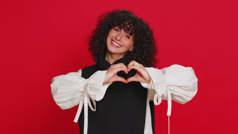 smiling young woman makes heart gesture demonstrates love sign expresses good feelings and sympathy