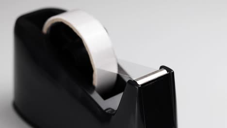 Person-taking-a-piece-of-sticky-tape-from-a-black-tape-dispenser