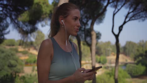 con el cabello atado en una cola de caballo, la chica en ropa deportiva se pone auriculares, enciende la música en su teléfono, y sonríe