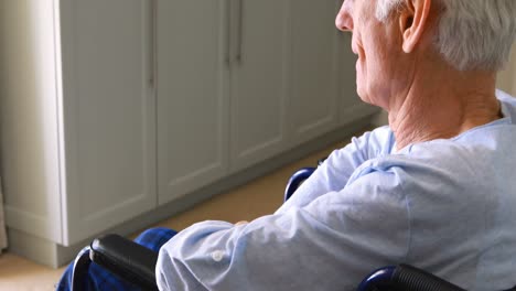 senior man sitting in wheelchair looking through window in bedroom