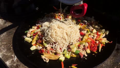 wok cooked outside in large pan, noodles being added