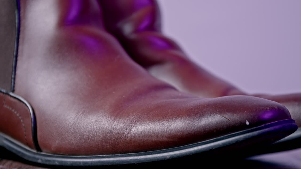 Detailed view of elegant leather boots showcasing rich texture with vibrant purple lighting. This close-up shot captures the essence of fashion and quality craftsmanship