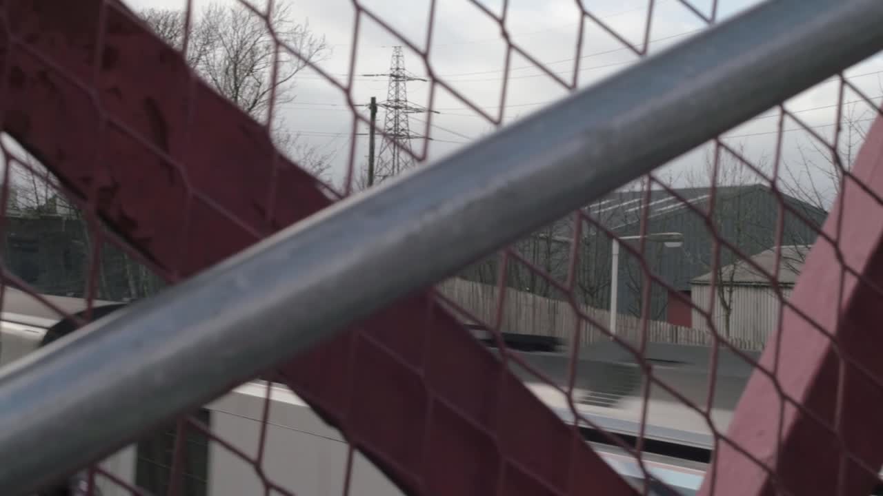 Fast moving train on tracks moving through station pov through fencing