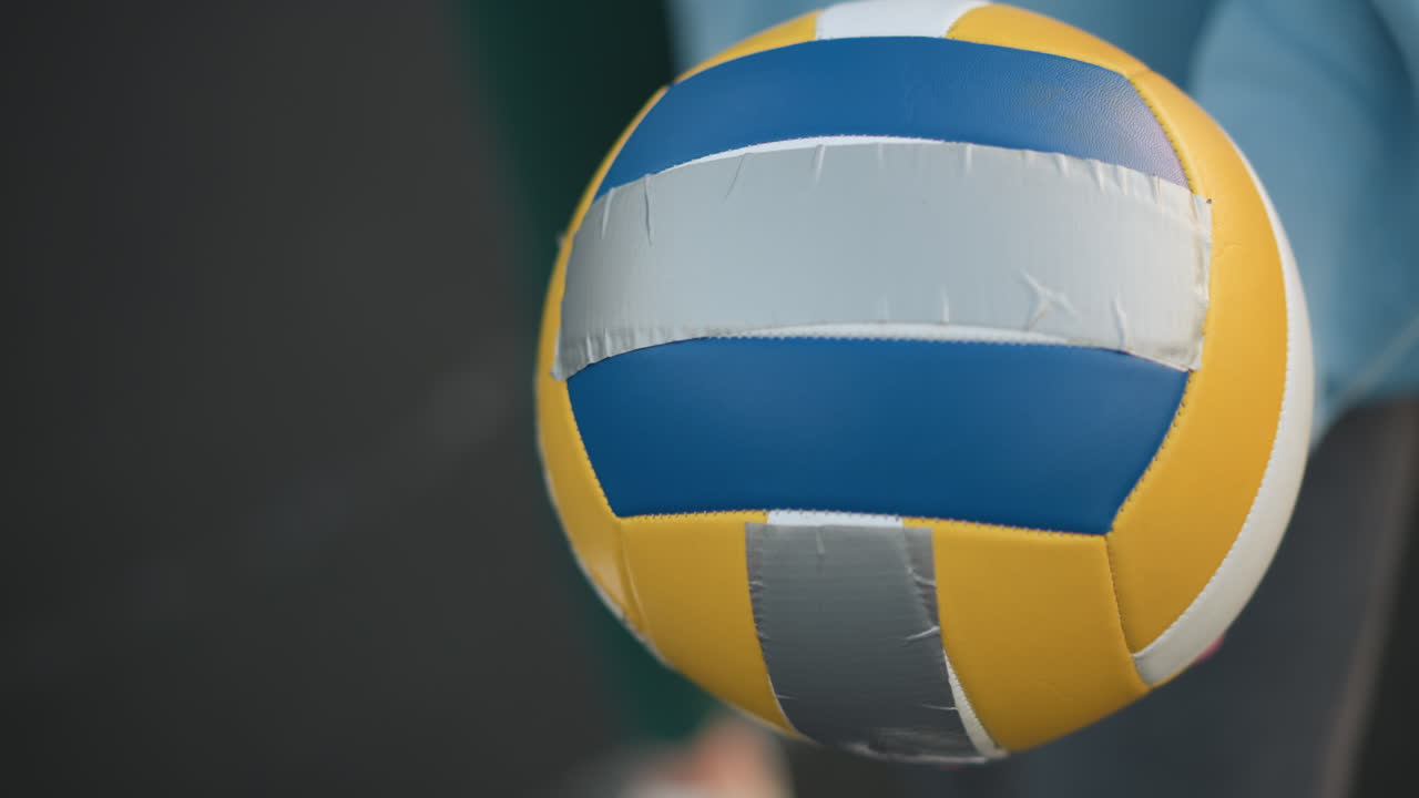 메룬 스웨터를 입은 다른 사람과 함께 여자 선수가 들고 있는 배구의 클로즈업으로, 둘 다 야외에서 기술을 배우고 연습하는 데 초점을 맞추고 있습니다.