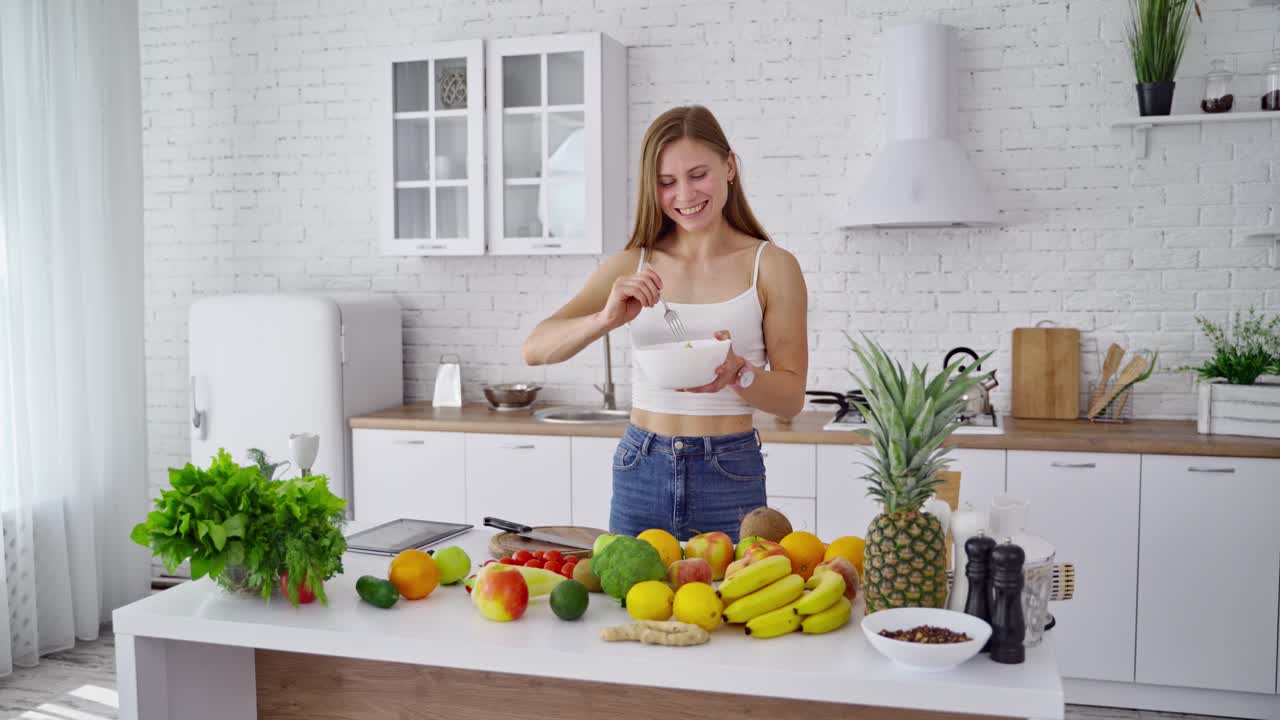 Woman with fresh salad in the kitchen. Attractive girl eating organic food at home. Beautiful housewife cooking salad. Healthy lifestyle.