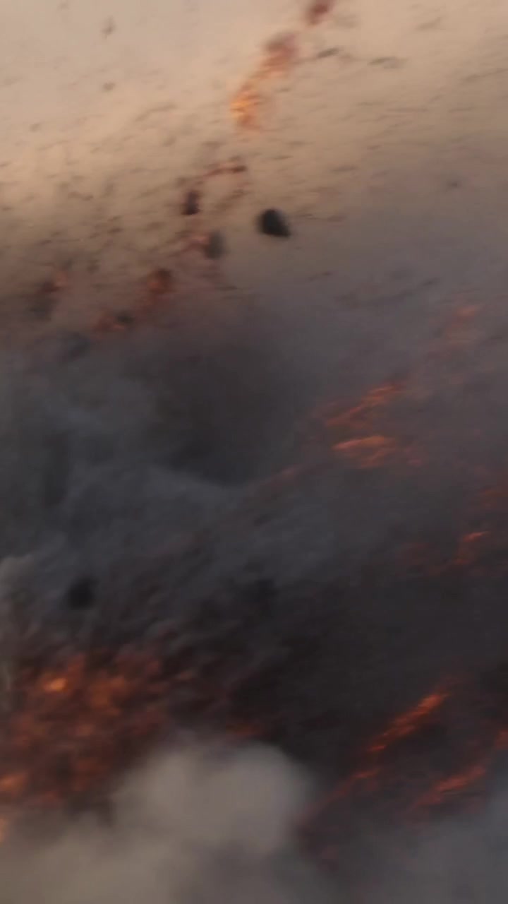 Vertical video: Rising smoke plume sending embers and falling ash from fire, wind lifting fragments