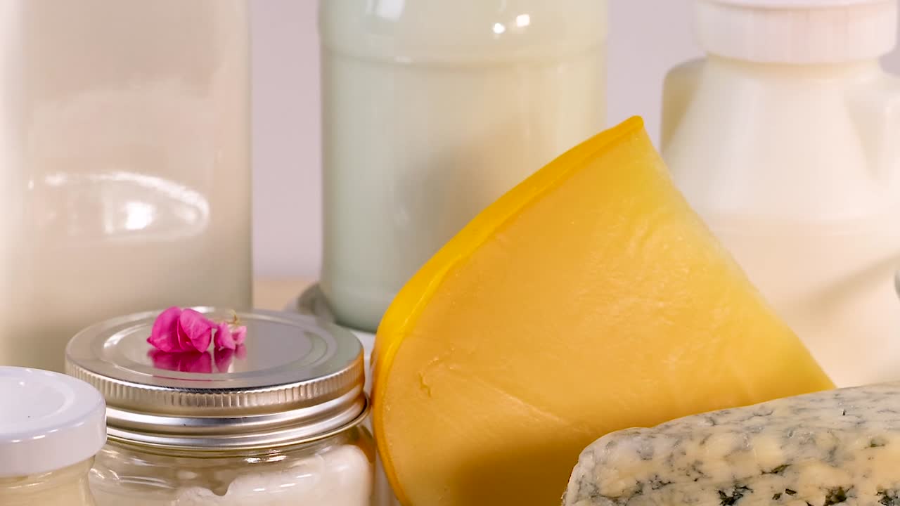 A selection of cheeses and milk bottles arranged on a white background with decorative herbs.