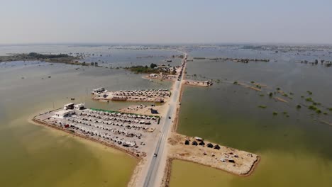 aerial view of lone elevated road with land housing makeshift camps for flood refugees surrounded by expansive flood waters in rural jacobabad, sindh