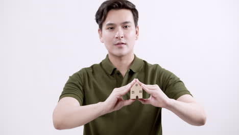 holding a miniature house, a young male model is advertising real estate properties in southeast asia.